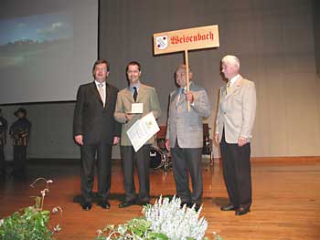 Bürgermeister Toni Huber nimmt mit Gärtnermeister Richard Strobel und dem ersten Vorsitzenden des Heimatpflegevereins Weisenbach, Richard Großmann, die „Silbermedaille“ in Empfang